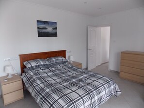 Une chambre à coucher avec un lit, une table de chevet, une commode et une porte.