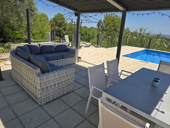 A covered outdoor seating area with a wicker sofa, a table, and chairs. - Modern villa with large private pool & far reaching sea views Catadau, Valencia (Catadau)