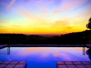 Ein Schwimmbad mit Blick auf einen Sonnenuntergang über einer hügeligen Landschaft.