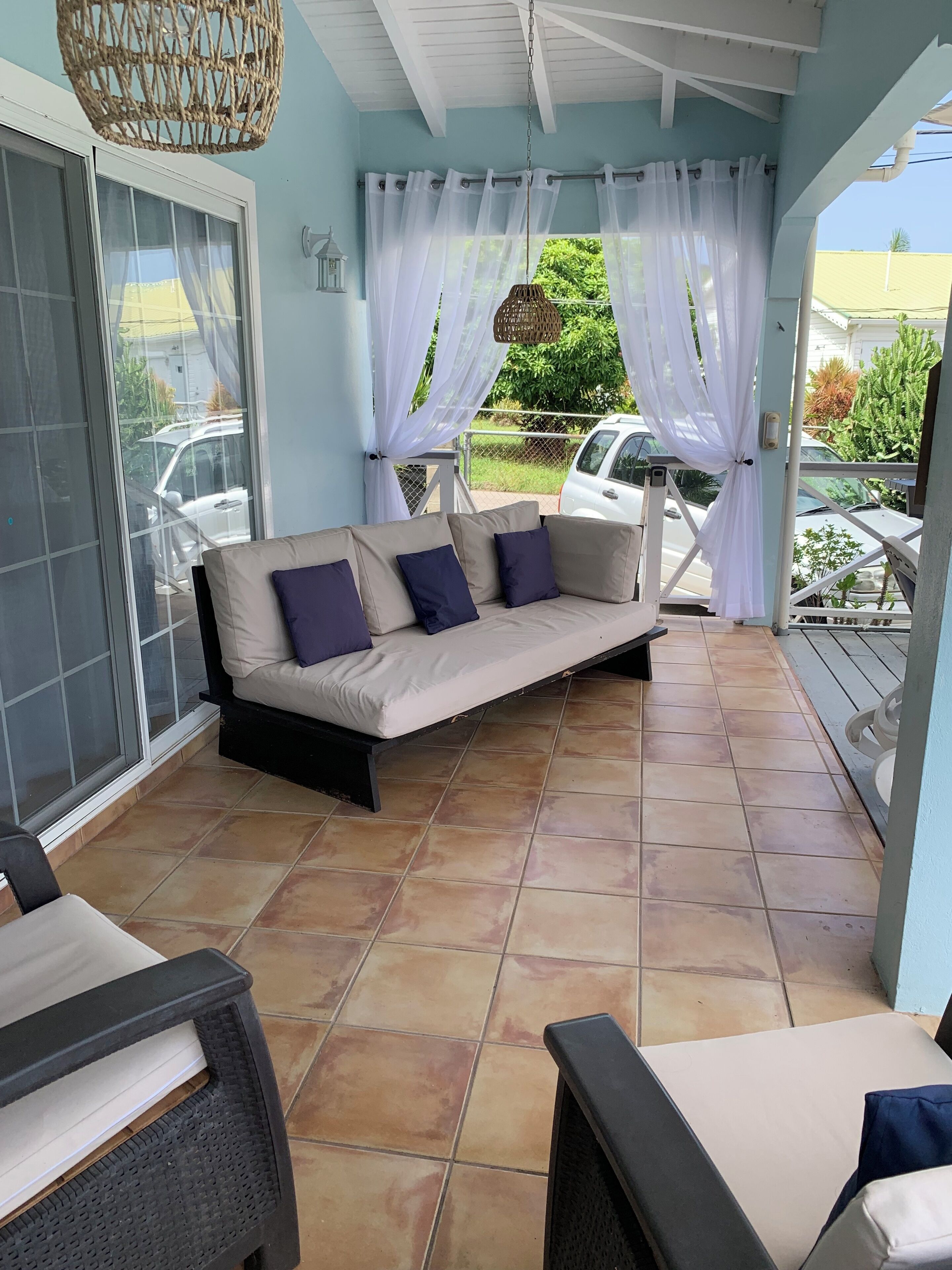 A covered patio area with a sofa, chairs, and a hanging light fixture.