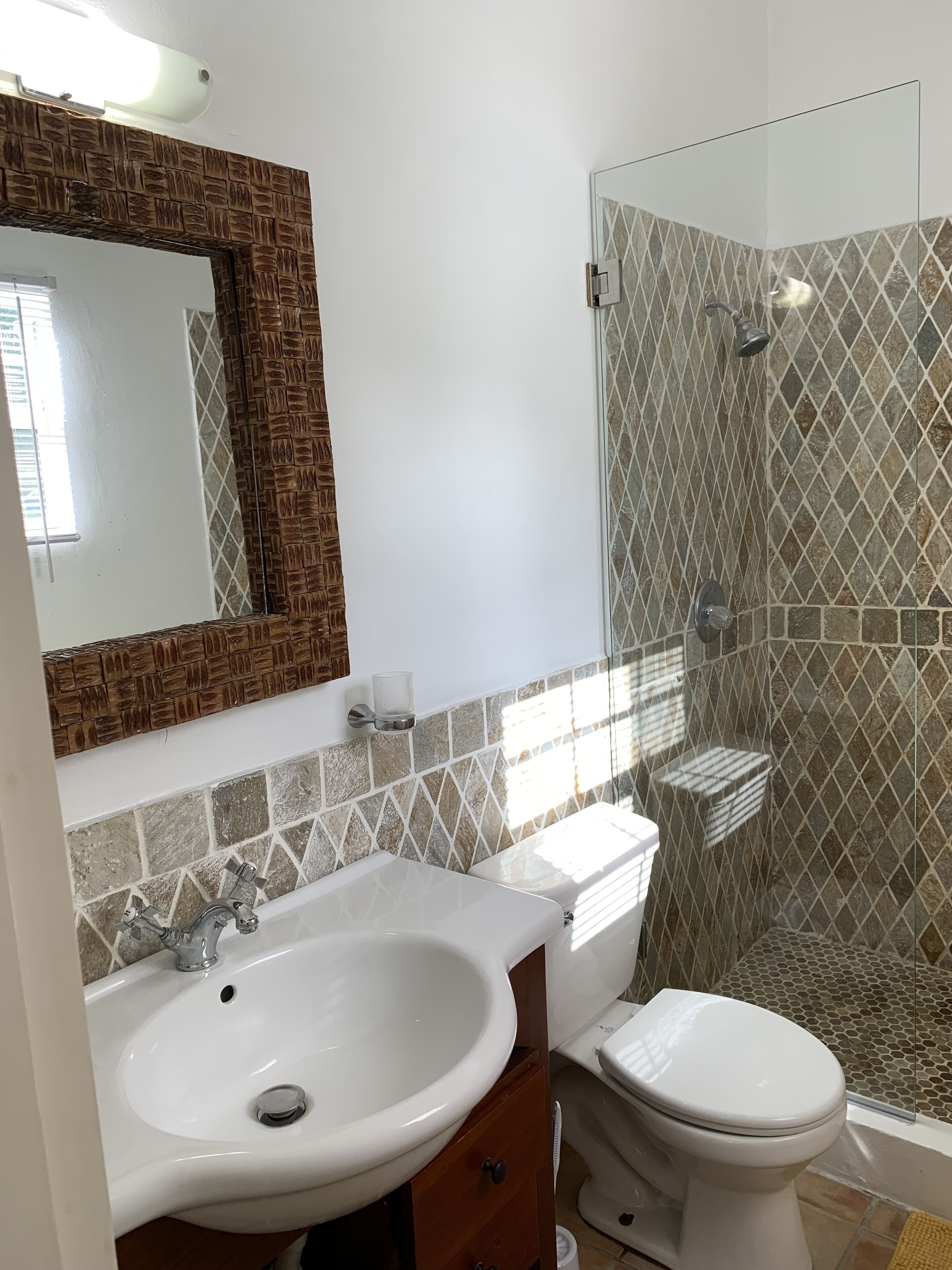 A bathroom with a white sink, a mirror with a wooden frame, a toilet, and a glass-enclosed shower area.