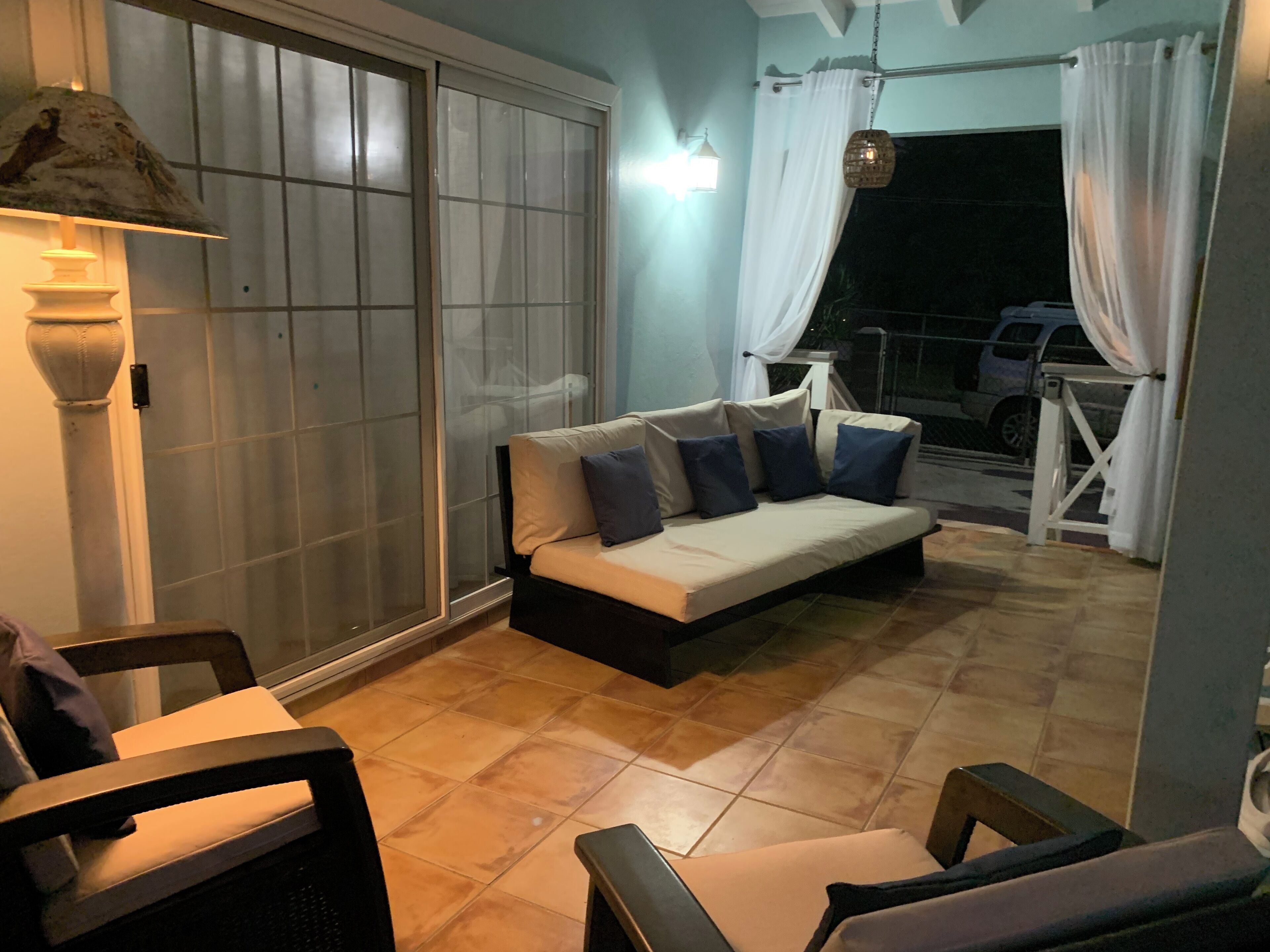 A cozy outdoor seating area with a sofa and chairs, a sliding glass door, and a view of a vehicle outside.