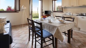 Un comedor con una mesa lista para dos personas, un sofá y un televisor al fondo.
