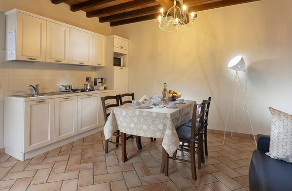 Una cocina compacta con armarios blancos, una mesa de comedor con mantel estampado y una lámpara de araña.