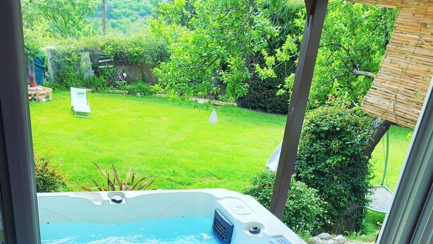Vista desde la ventana a un jacuzzi, con césped y árboles al fondo.