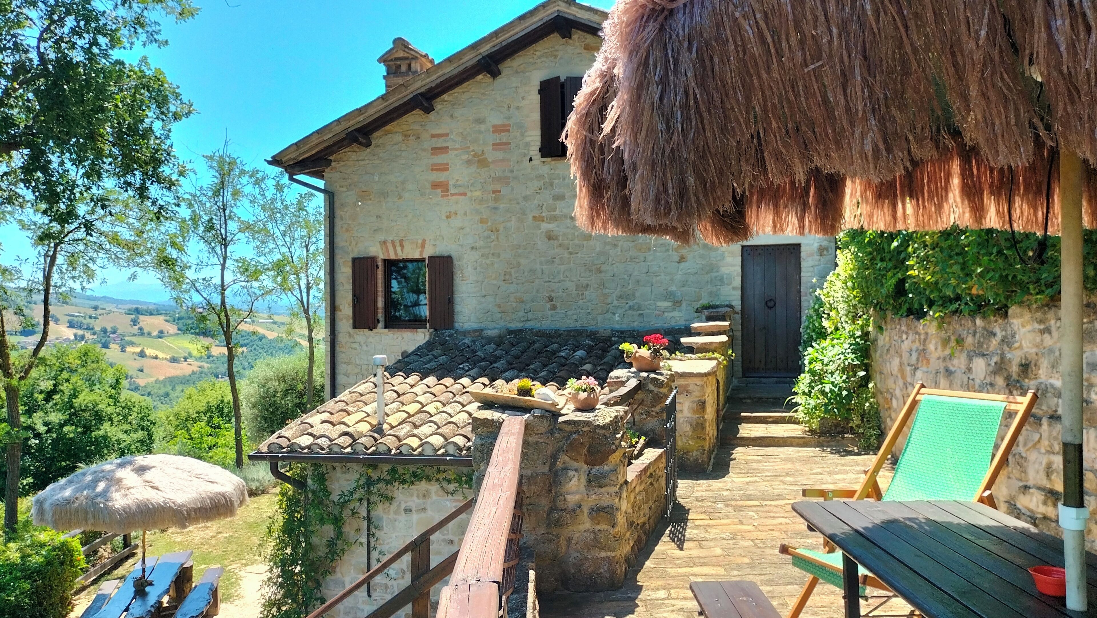 A stone house with a tiled roof, a wooden deck, and a thatched roof structure.