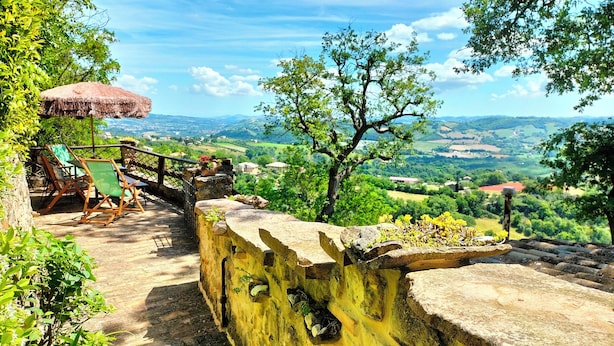 Un banco de piedra con vistas a un valle, una sombrilla rústica y una silla de madera.