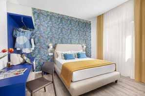 Ein Hotelzimmer mit einem Bett, einem Schreibtisch mit Stuhl, einem Kleiderschrank und floralem Wandpapier.