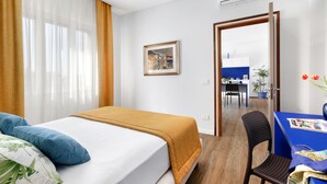 A hotel room with a bed, a desk, and a chair. There is a window with curtains, a painting on the wall, and an air conditioning unit. - Sea View Apartment on the bay of Naples last minutes discount 25 - 30 june (Castellammare di Stabia)