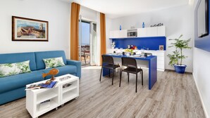 A modern living room with a blue sofa, a dining area with two chairs, and a kitchen with blue cabinets. - Sea View Apartment on the bay of Naples last minutes discount 25 - 30 june (Castellammare di Stabia)