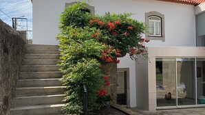 Un edificio con techo de tejas rojas, una escalera que lleva a una puerta y un jardín con plantas y flores en macetas.