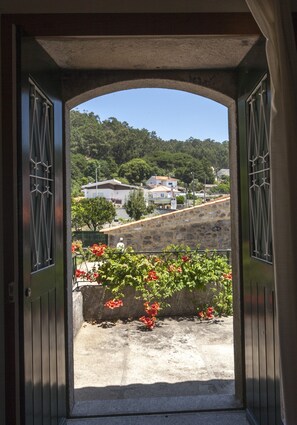 Une porte donnant sur un balcon d’où l’on peut admirer une colline et des maisons.