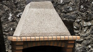 Un horno de ladrillo al aire libre con techo inclinado y chimenea, frente a un fondo rocoso.
