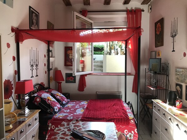 Une chambre à coucher avec un lit à baldaquin, une fenêtre avec des rideaux, une commode et un téléviseur posé sur un meuble.
