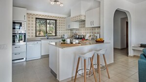 A modern kitchen with white cabinetry, a central island with stools, and a window with a view of greenery. - Villa Susana ~ Heated Pool* ~ Fast Wi-fi ~ 6 + 4 cots - Booking 2027 & 2028 NOW! (Sao Bartolomeu de Messines)