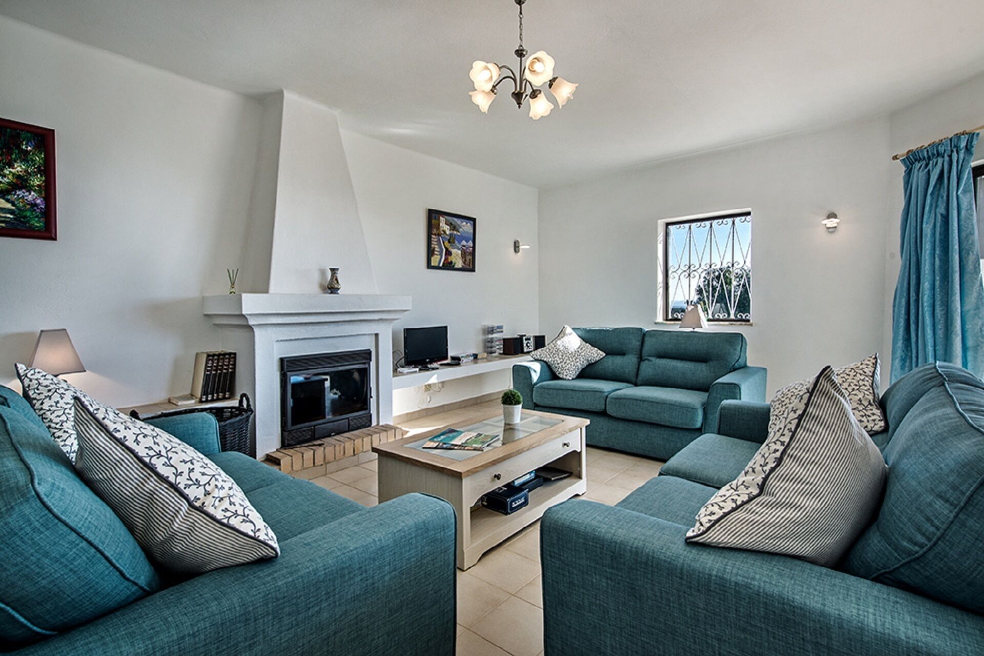 Ein modernes Wohnzimmer mit türkisfarbenen Sofas, einem Kamin, einem Couchtisch und einer Deckenleuchte.