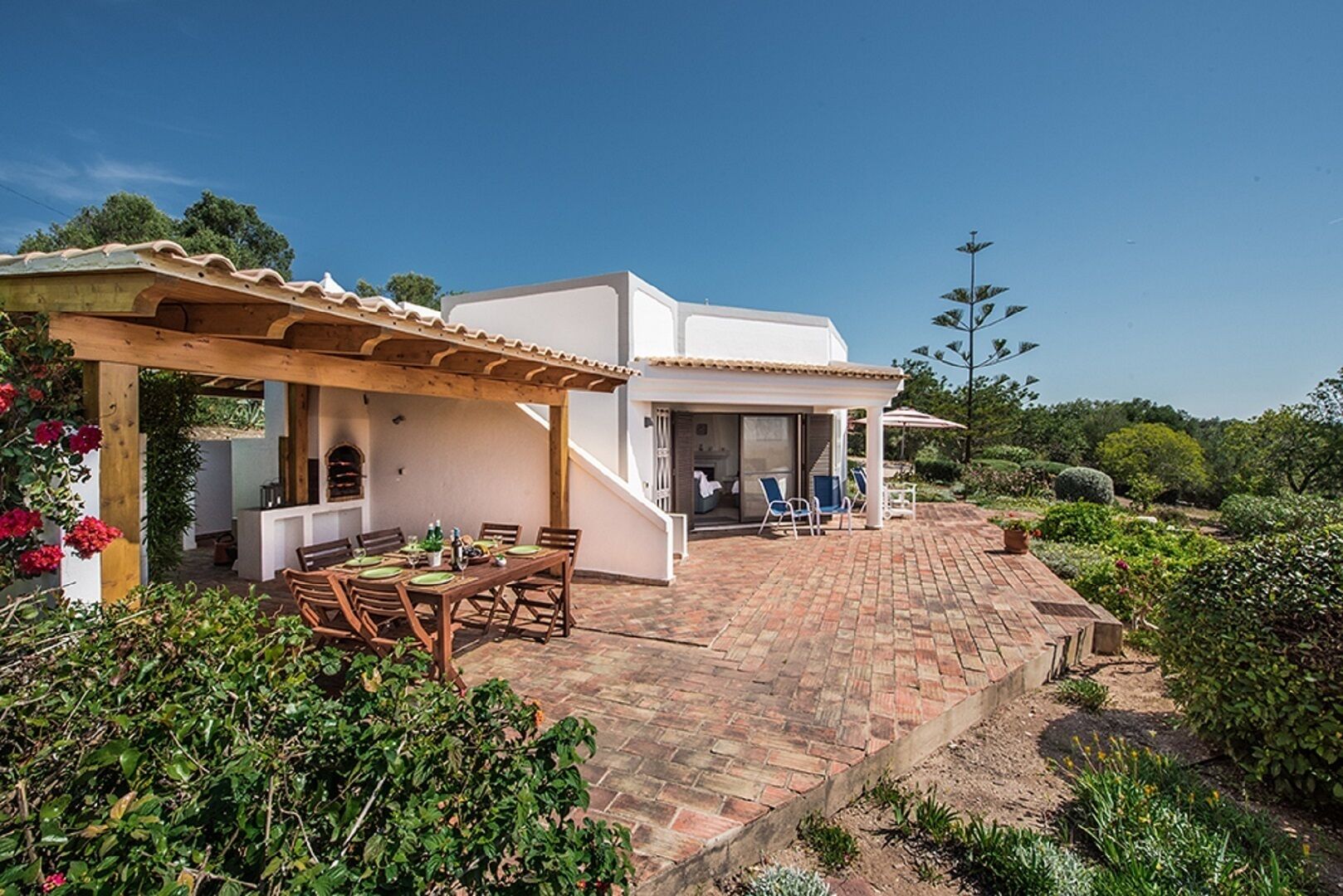 Ein Haus mit einer Terrasse, einem überdachten Essbereich und einem Garten.