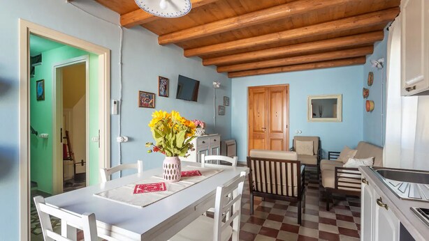 A cozy kitchen with a wooden ceiling, a dining area with a table and chairs, and a living area with a sofa and a TV. - Ancient Mansion of the Arcolaio - F4856 (Nurachi)
