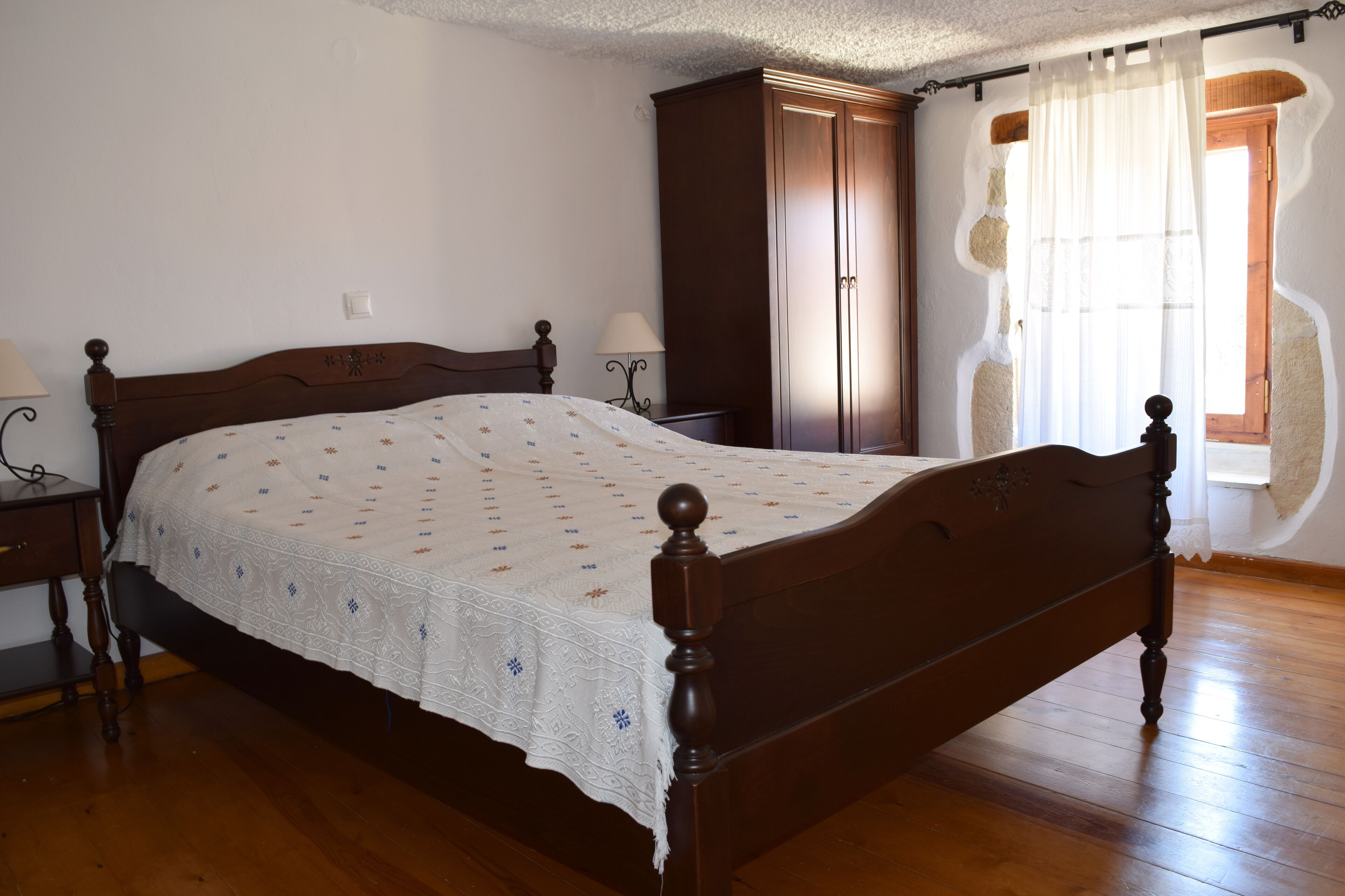 A bedroom with a wooden bed, a wardrobe, and a nightstand with a lamp.