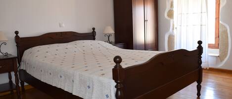 A bedroom with a wooden bed, a wardrobe, and a nightstand with a lamp.