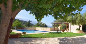 Zona de piscina con patio de piedra, césped y una pérgola con vistas a las montañas.