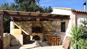 A stone-floored patio with a wooden pergola, a stone fireplace, and a table with chairs.