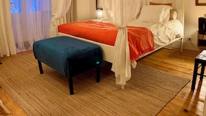 Une chambre à coucher avec un lit à baldaquin, une table de chevet, une chaise, une fenêtre avec des rideaux et un ventilateur de plafond.