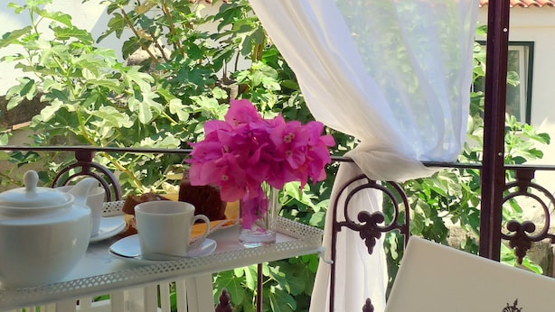 Un balcon avec une table préparée pour le thé, entouré de verdure et agrémenté d’une chaise blanche.