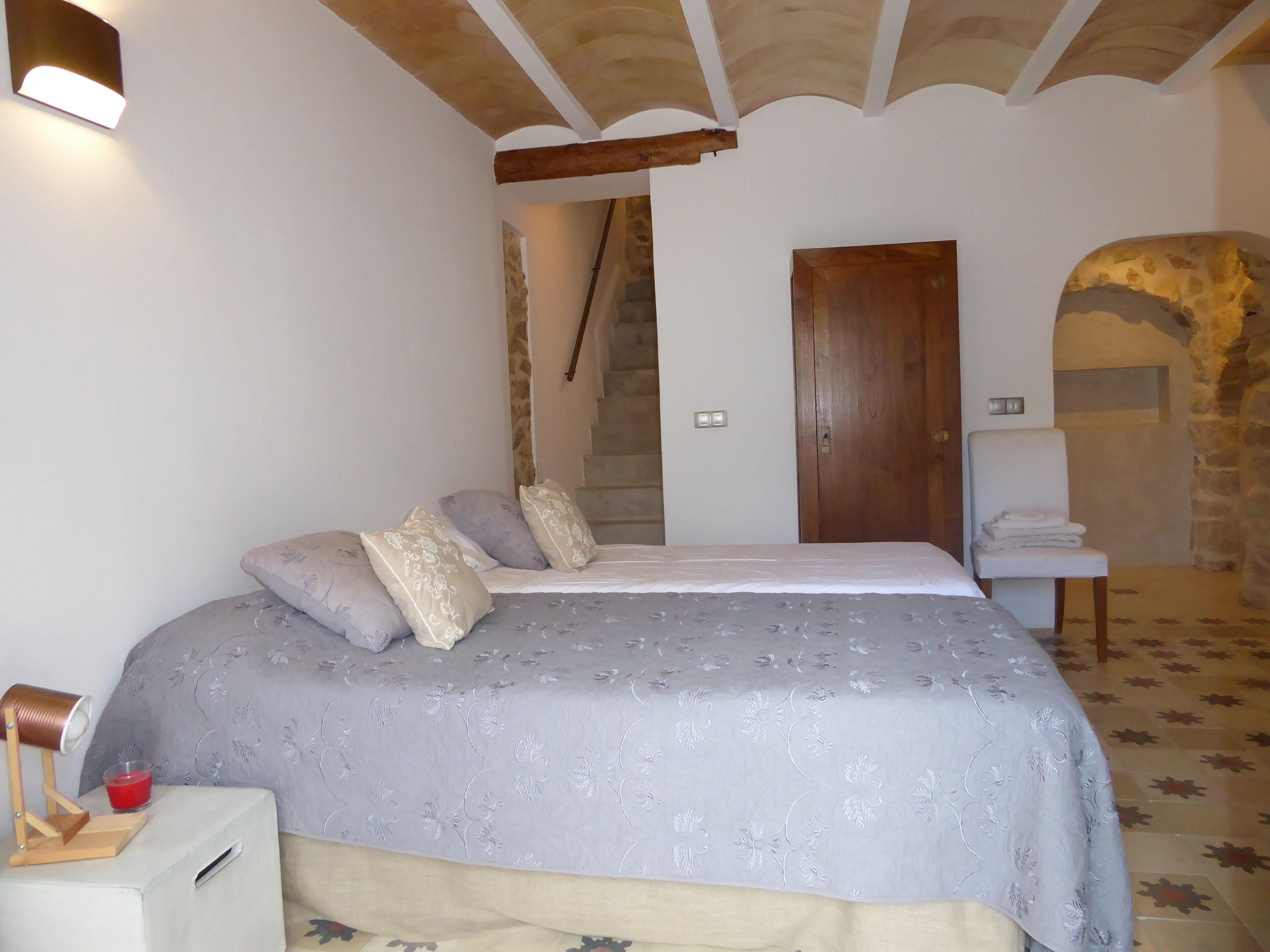 Une chambre à coucher avec un lit, une table de chevet, une lampe, une bougie rouge et un mur en pierre.