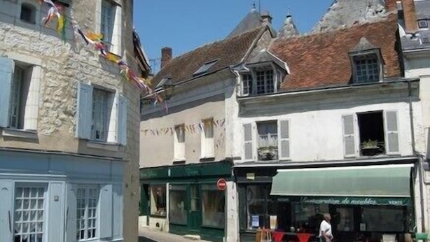 Una stretta via fiancheggiata da edifici storici, uno dei quali presenta una vetrina e un altro un cartello con la scritta "Véritabletion de meubles".