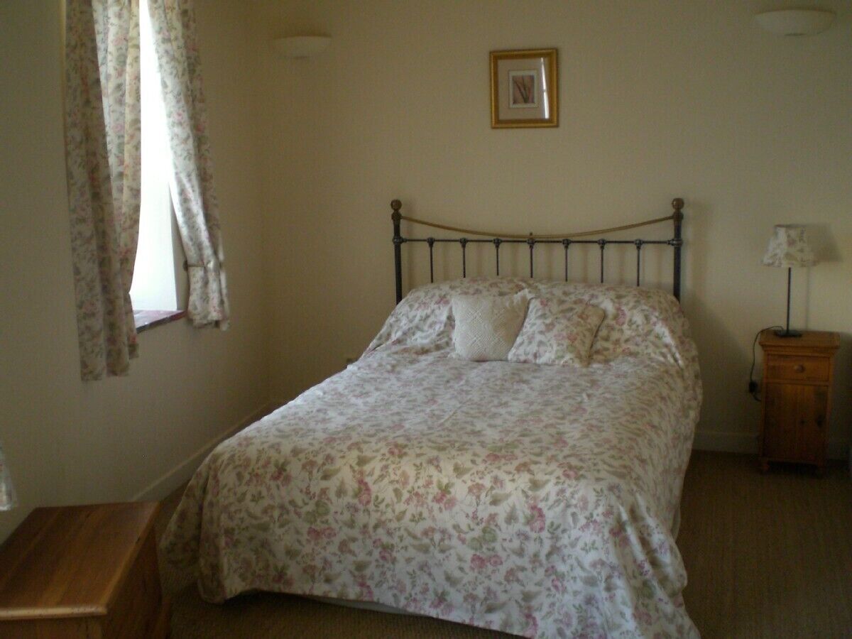 Une chambre à coucher avec un lit, une table de chevet, une lampe et une fenêtre avec des rideaux.