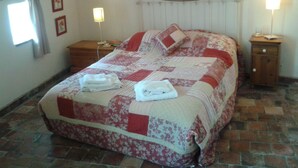Un letto rifatto con una coperta a fiori, un comodino con una lampada e un tavolino da notte illuminato.