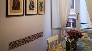Un coin repas avec une table dressée pour deux personnes, des œuvres d’art encadrées au mur et une fenêtre avec des rideaux.