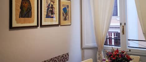 Uma área de refeições com uma mesa posta para dois, obras de arte nas paredes e uma janela com cortinas.