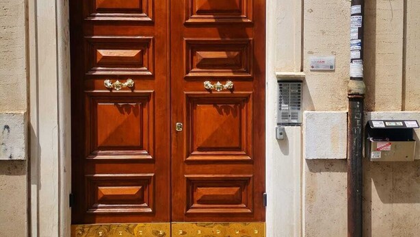 Une porte en bois à deux vantaux, ornée d’un panneau décoratif dans sa partie inférieure, le chiffre « 3 » peint sur le mur, et un coffret de raccordement électrique sur la droite.