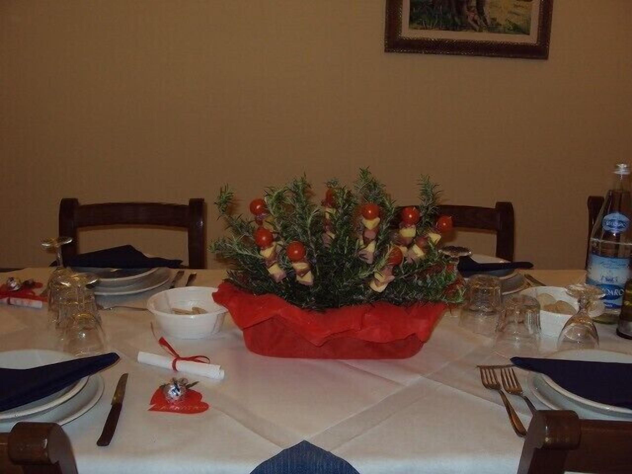 Une table à manger dressée pour un repas, agrémentée d’un centre de table composé d’un arrangement floral rouge et d’un petit sapin de Noël.