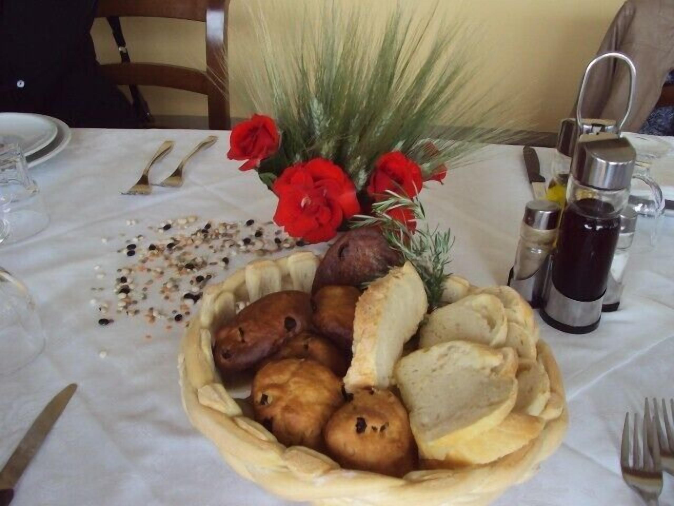 Une table avec un panier de viennoiseries, un vase de fleurs rouges et une cafetière.