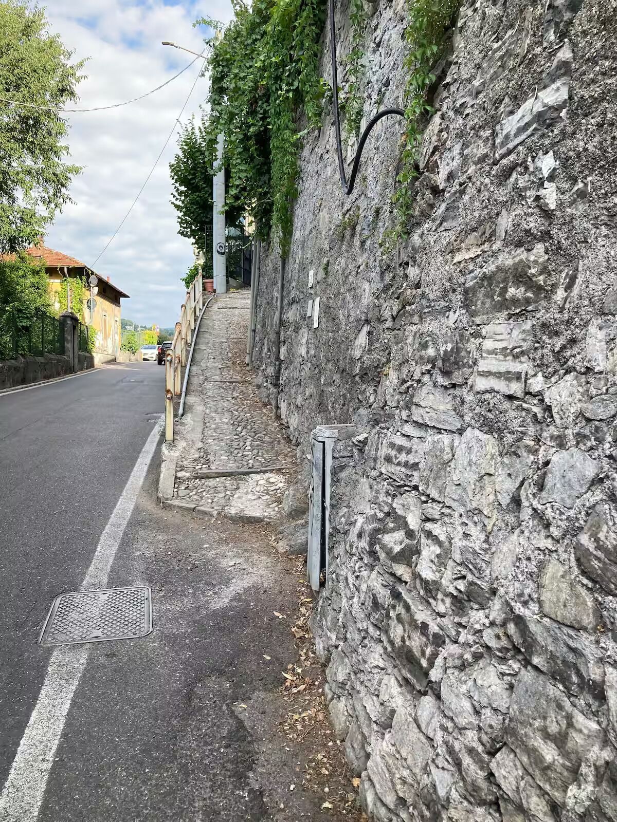 A narrow street with a stone wall on one side and a paved road on the other.