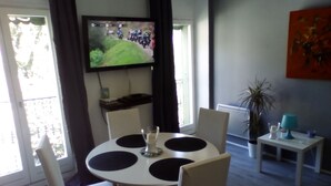 Zona pranzo con tavolo rotondo, sedie e televisore fissato alla parete.
