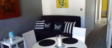 A modern living room with a black and white sofa, a round table with black circular mats, and a small side table with a blue lamp.