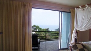 Une chambre avec un lit, une chaise et un balcon donnant sur l’océan.