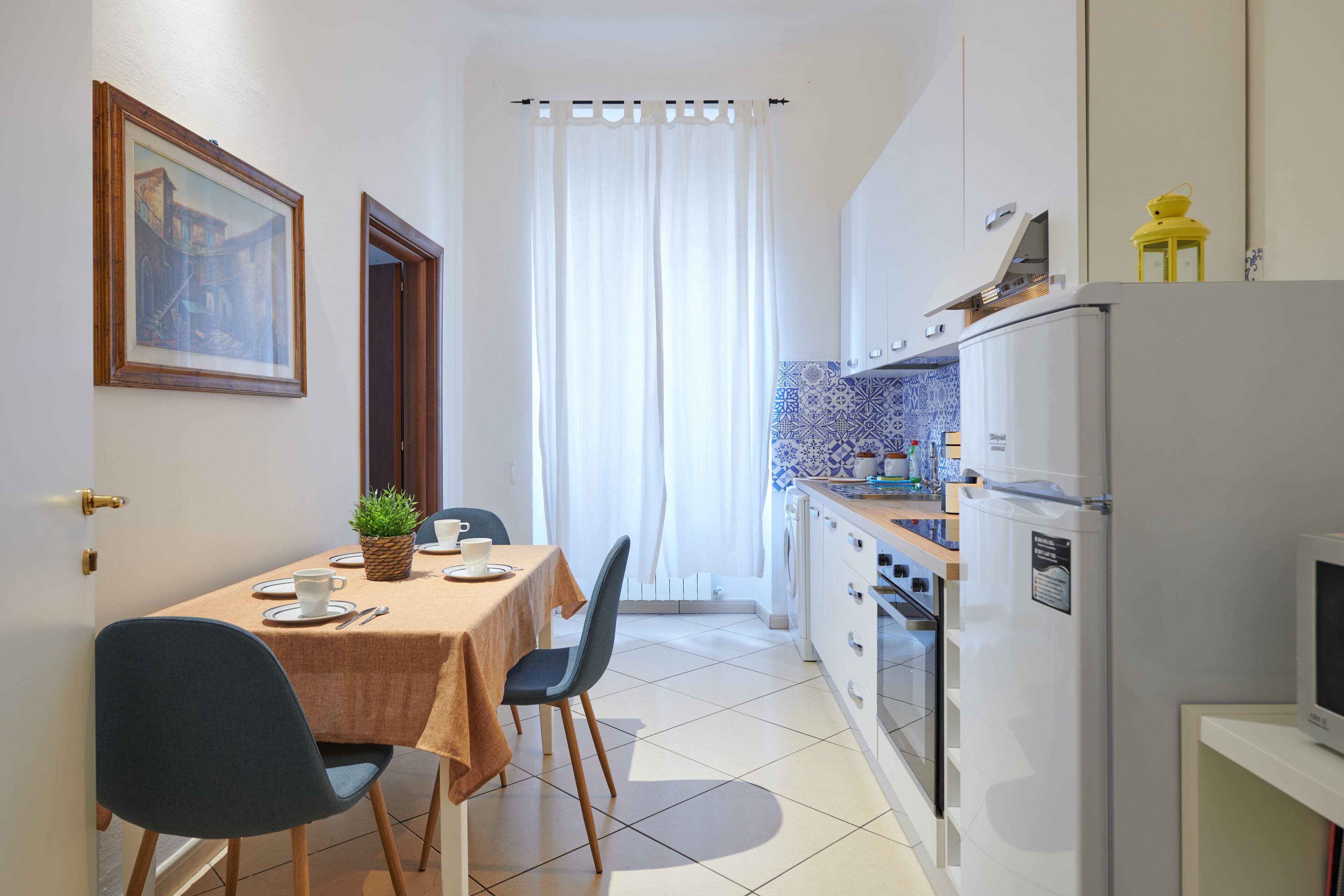 Une cuisine compacte avec un coin repas, comprenant une table dressée pour deux personnes, des chaises, un réfrigérateur et un four à micro-ondes.