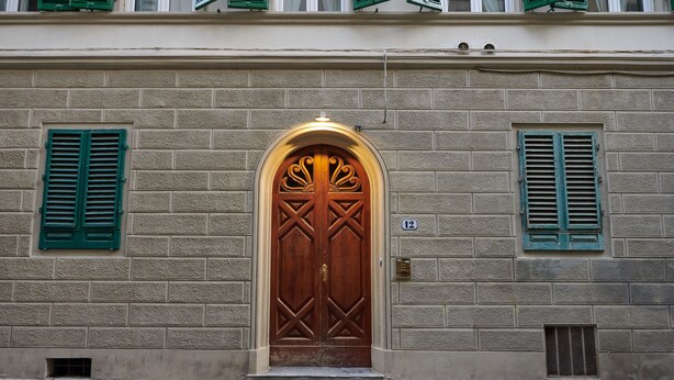 A building with a large wooden door, green shutters, and a brick facade. - Characteristic Apartment in the City Center of Florence (Firenze)