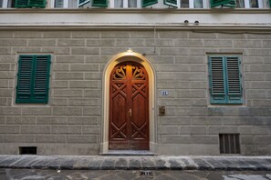 A building with a large wooden door, green shutters, and a brick facade. - Characteristic Apartment in the City Center of Florence (Firenze)