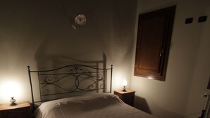 Un dormitorio tenuemente iluminado con una cama de estructura metálica, una mesita de noche con una lámpara y un armario de madera en la pared.
