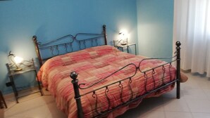 Une chambre à coucher avec un lit en métal, une couvre-lit à carreaux, une table de chevet avec une lampe et un tableau accroché au mur.