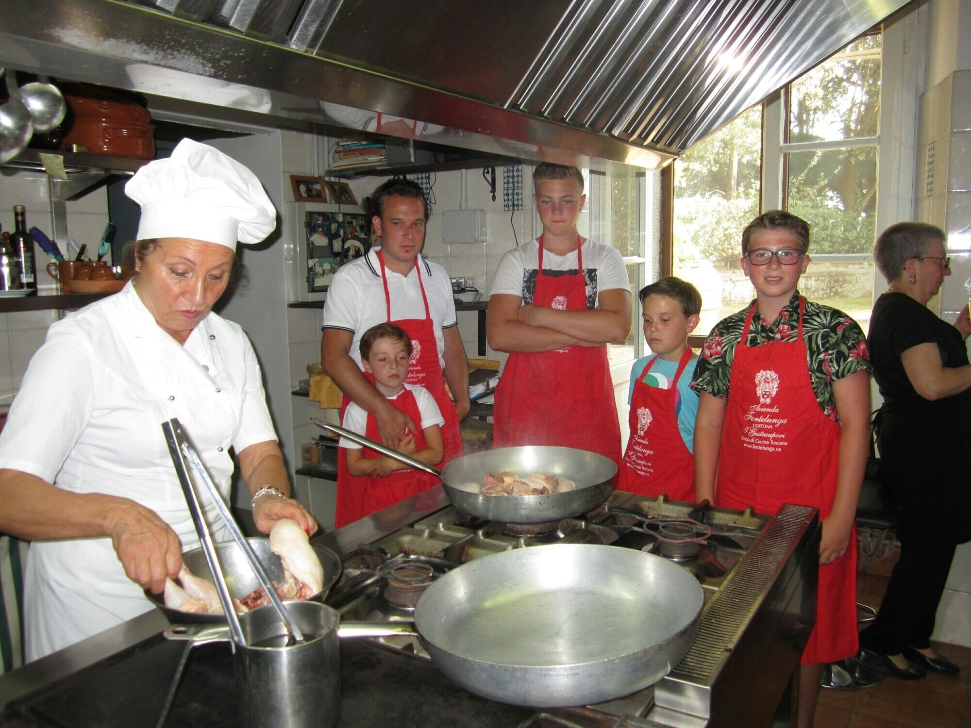 Une cuisine où un chef prépare des plats, plusieurs personnes portant des tabliers et divers ustensiles de cuisine.