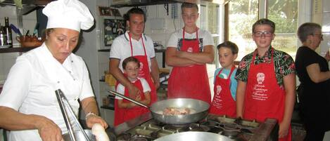 Une cuisine où un chef prépare des plats, plusieurs personnes portant des tabliers et divers ustensiles de cuisine.
