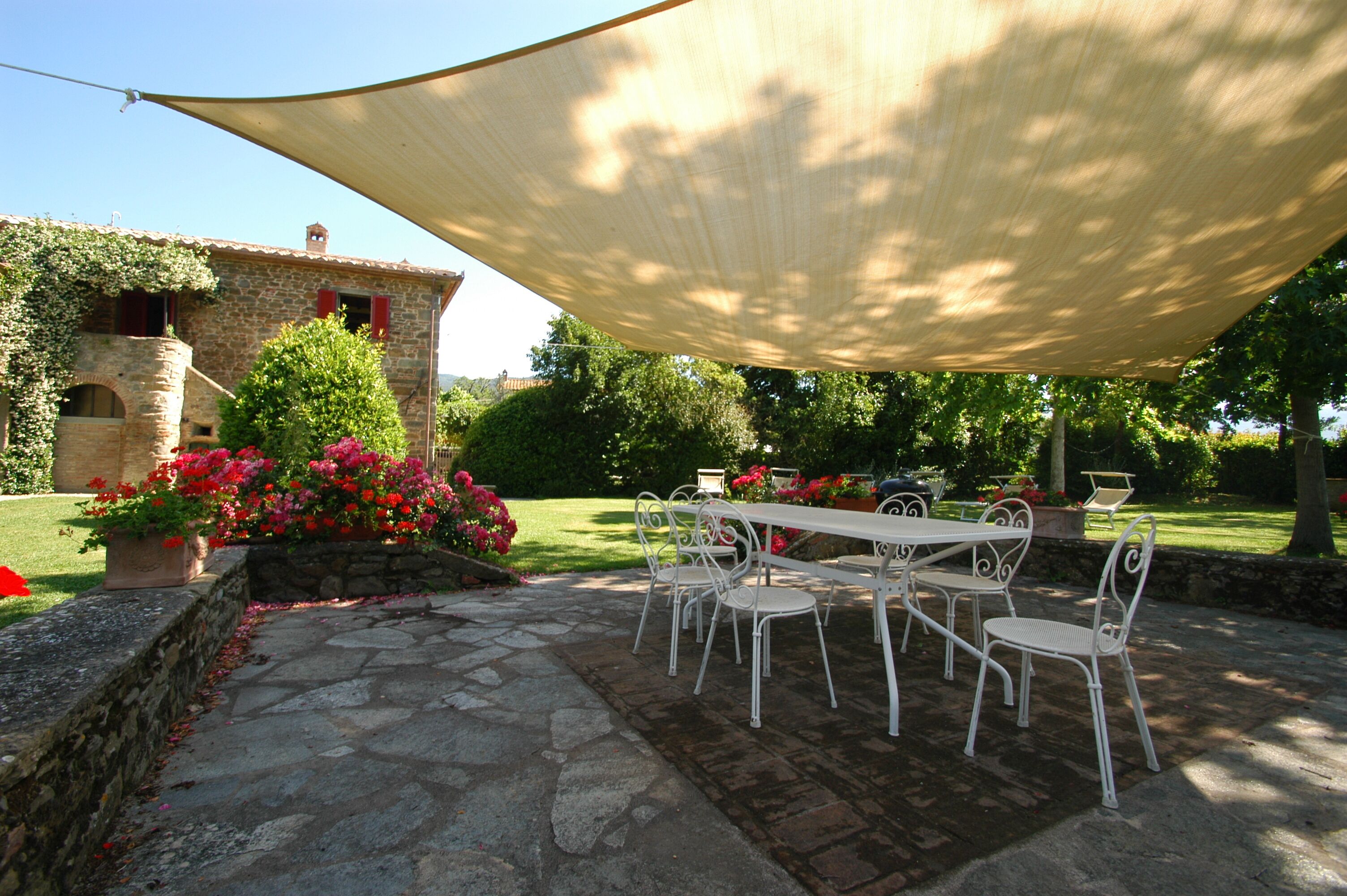 Un patio exterior con una mesa y sillas, un sendero de piedra y un edificio con techo inclinado y contraventanas rojas.