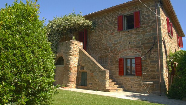 A stone building with red shutters, a small staircase, and a grassy area in front. - Lovely, spacious independent apartment in Tuscan Farmhouse (Cortona)